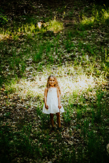 Vertical portrait of young girl standing on hill in forest.