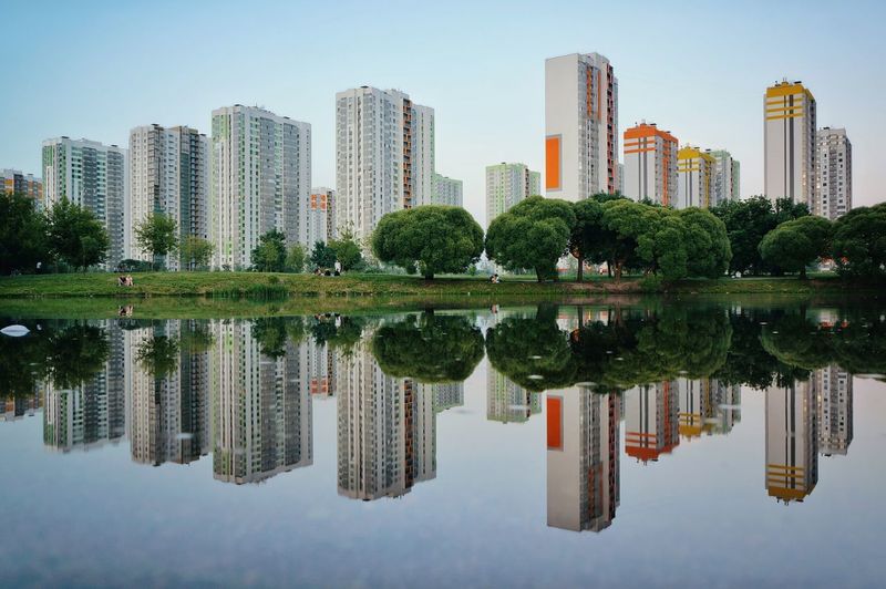 Reflection of buildings in calm lake against clear sky