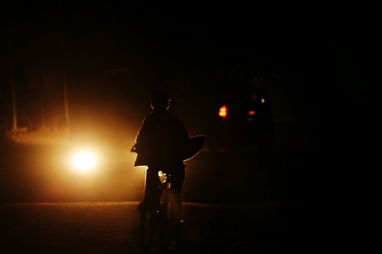 Silhouette man bicycling on road at night