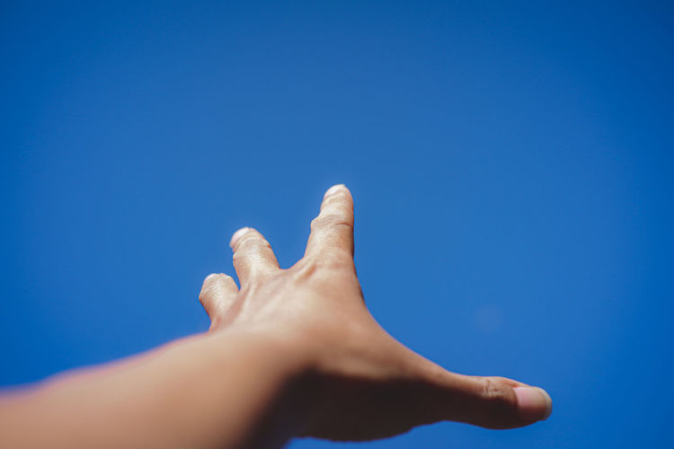Low angle view of person hand against clear blue sky