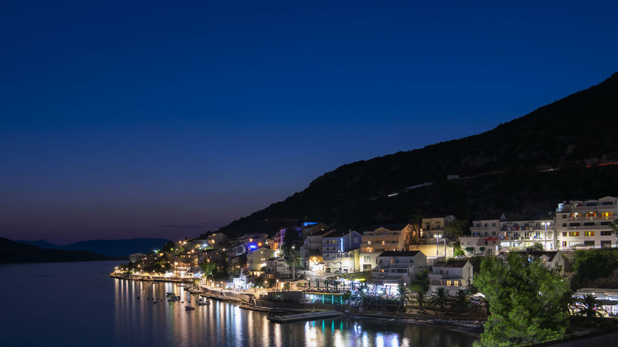 Illuminated city by sea against clear sky at night