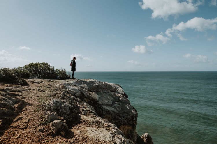 Side view of woman standing on cliff by sea against sky