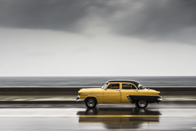 Car on road against sea and cloudy sky