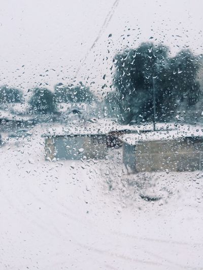 Snow covered street and houses seen through wet window