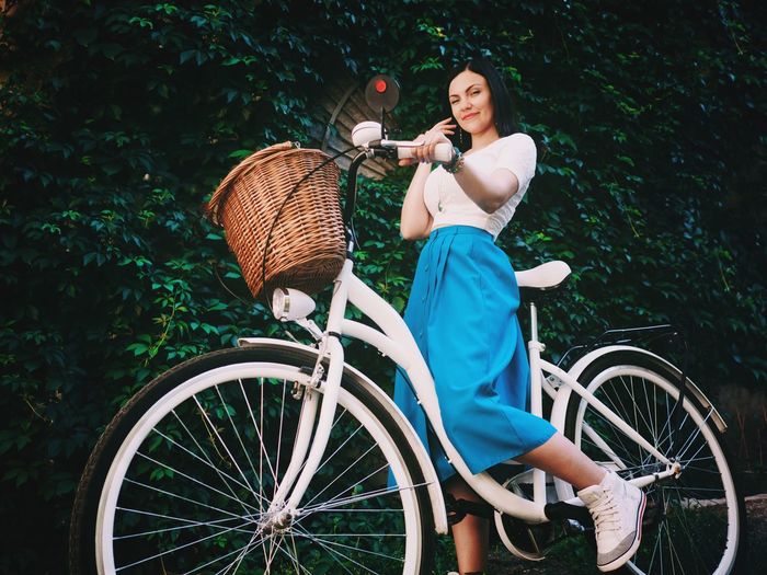 Low angle portrait of beautiful woman with bicycle against ivy