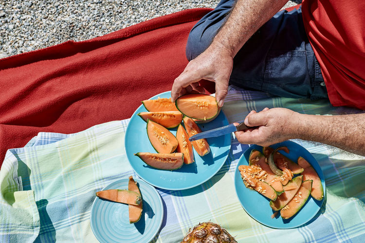 Middle aged couple having a picnic at the seaside with fresh exotic fruit. man cuts a melon. 