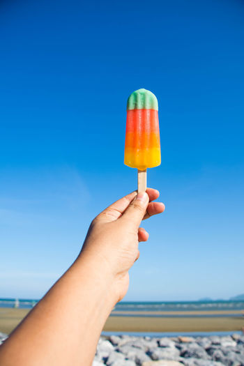 Cropped image of person holding flavored ice cream against sky