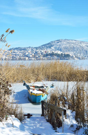 Snowy lake scene with boat trapped in the lake and town of kastoria as background
