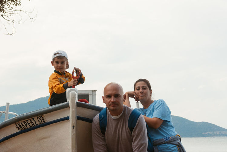 Portrait of father and mother with son in boat against clear sky at shore