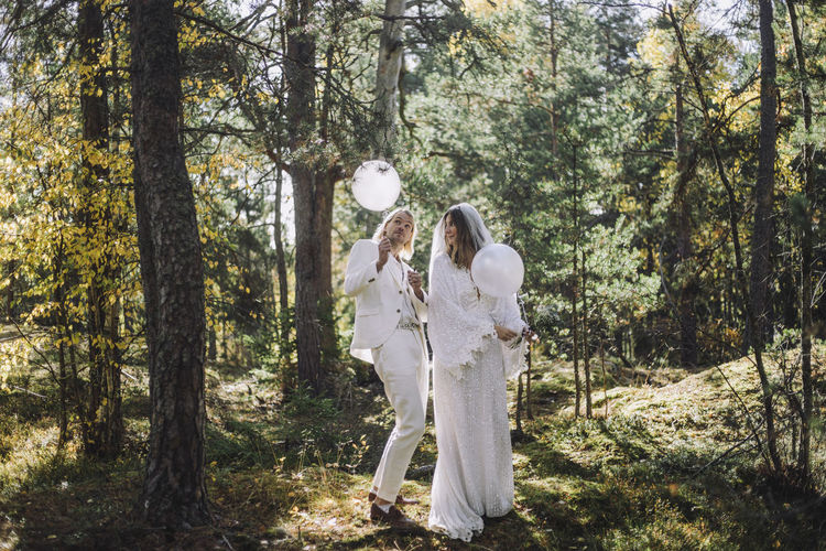 Mid adult couple playing with white helium balloons in forest