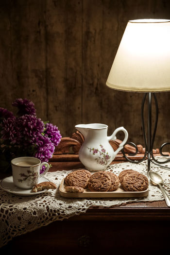 Homemade cookies with coffee on rustic table illuminated with a lamp