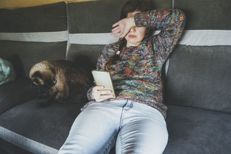 Tired woman with smart phone sitting on sofa