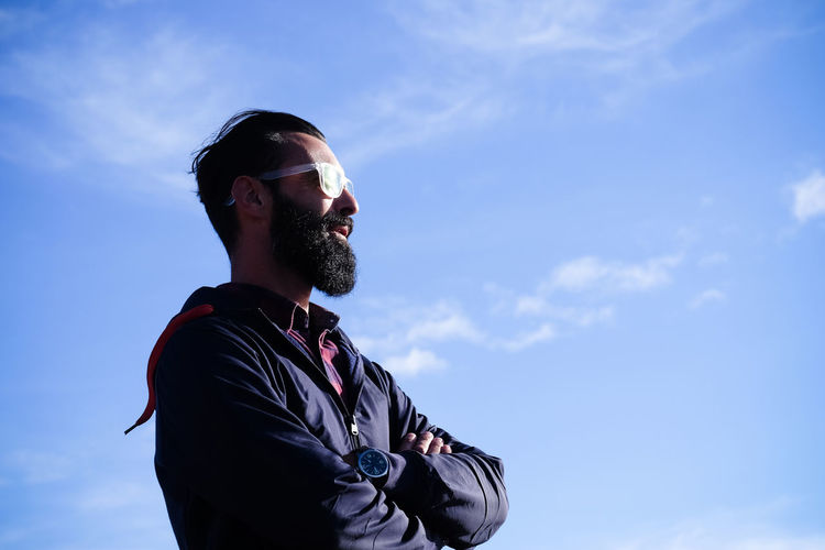 Portrait of man with full beard and sunglasses in front of sky