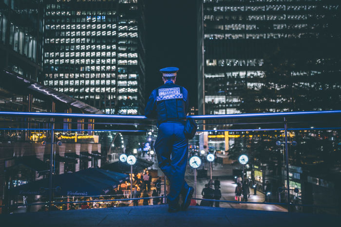Security officer standing on bridge while looking at illuminated city during night