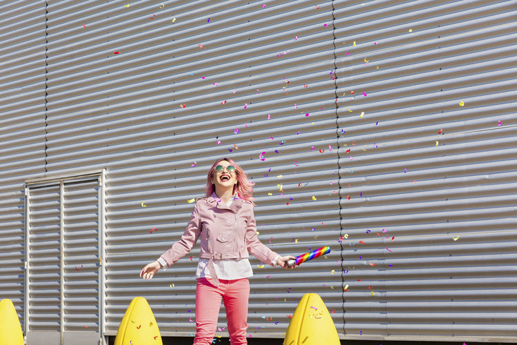 Cheerful woman with party popper having fun while falling confetti during sunny day