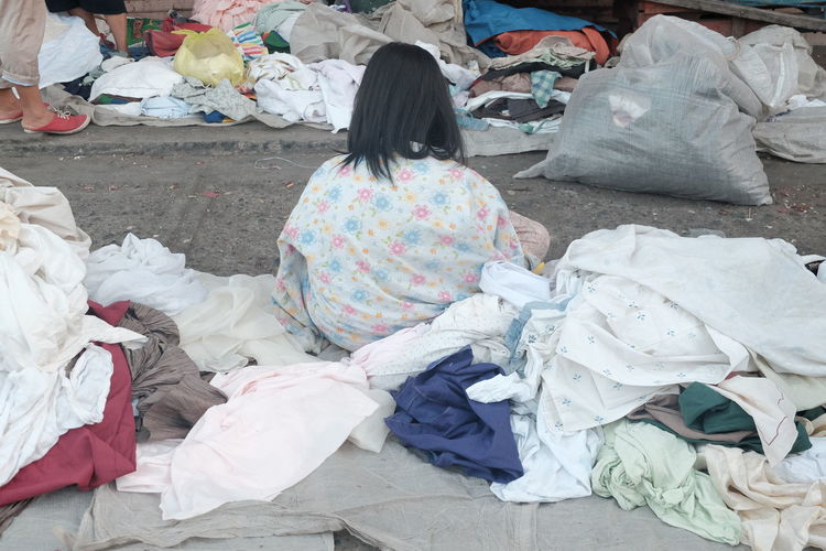 Rear view of homeless woman with stacked clothes on footpath