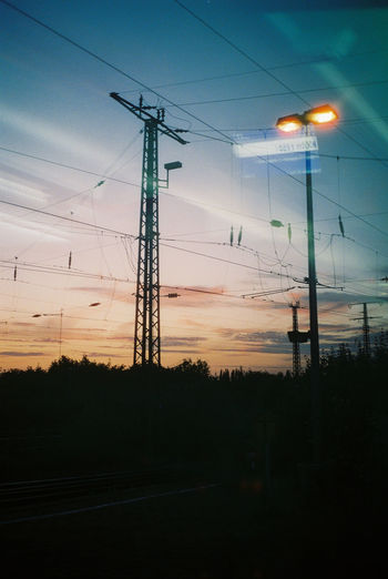 Low angle view of electricity pylons against sky at sunset