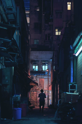 Rear view of man walking on alley amidst buildings in city
