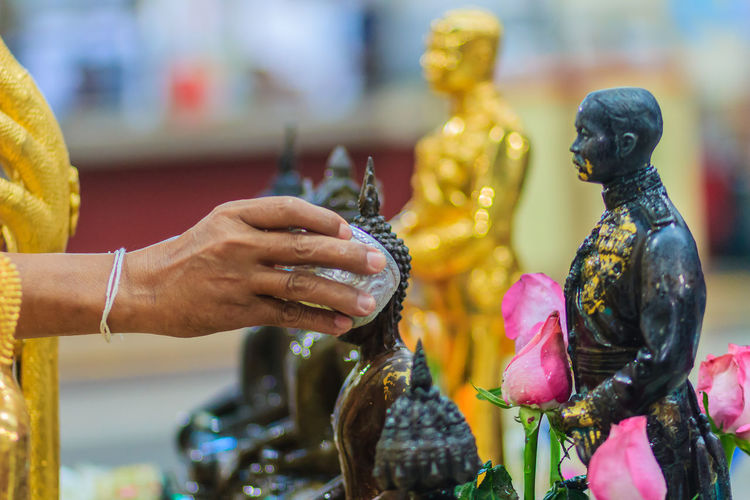 Cropped image of hand pouring water on buddha statue