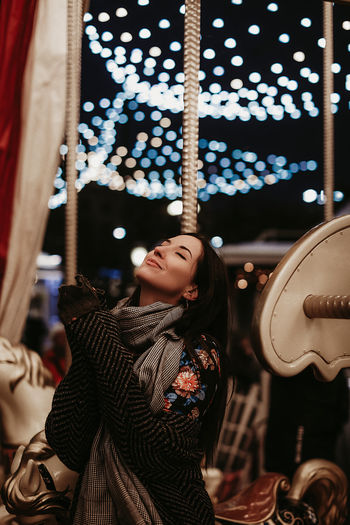 Young woman in cozy winter knitted scarf against the background of a silver blue sparkling carousel