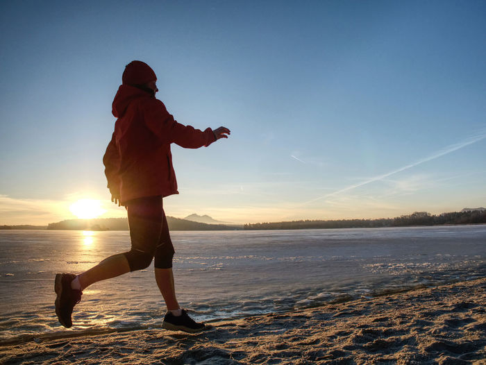 Winter running training. middle age active woman runner jogging in short leggings at frozen sea