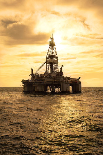 Oil rig in sea against cloudy sky