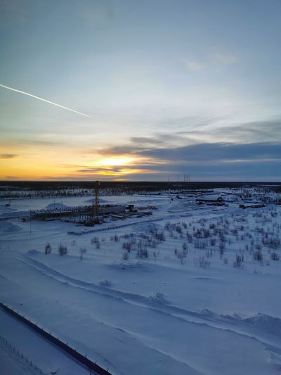 Snow covered shore against sky during sunset