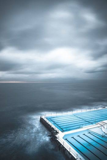 Scenic view of swimming pool by sea against cloudy sky