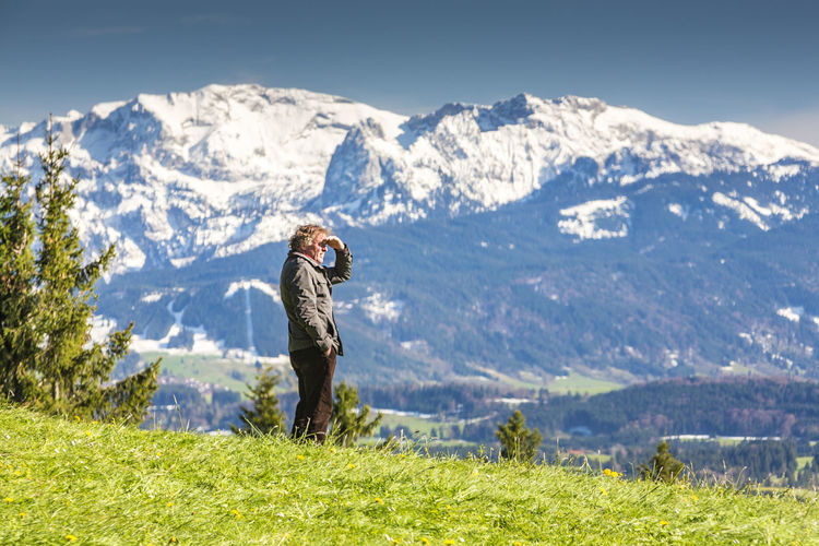 Man standing on grassy field against snowcapped mountains