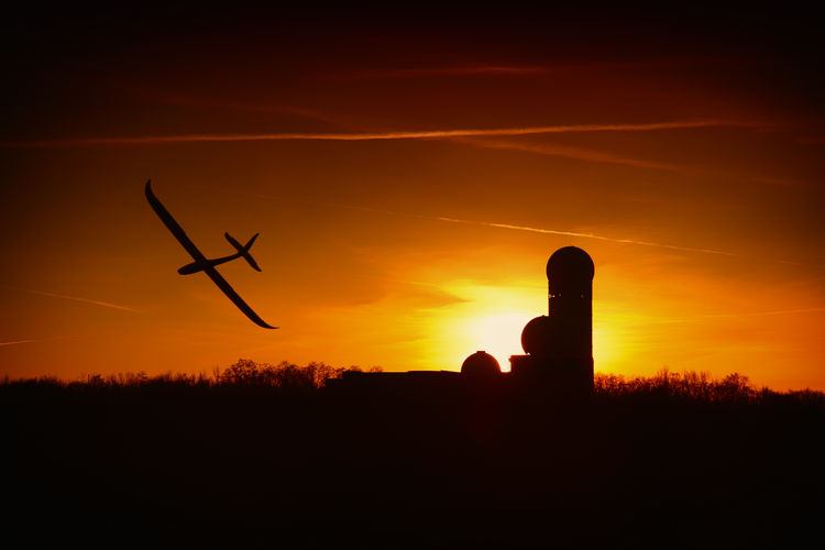 Silhouette airplane flying against sky during sunset