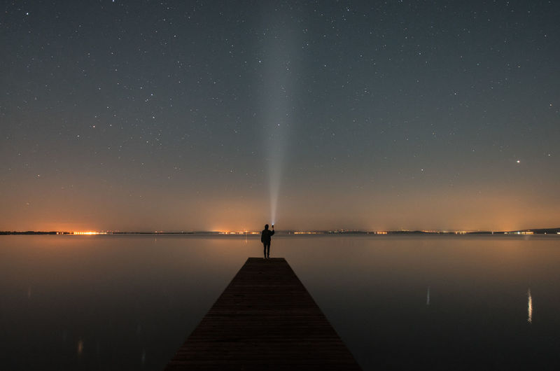 Man standing on pier over lake against sky at night