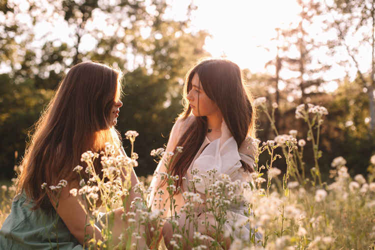 Lesbian couple talking sitting amidst flowers in summer forest