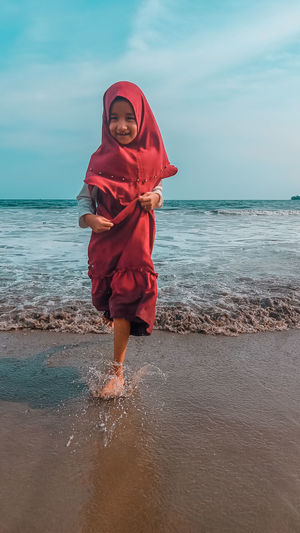 Full length portrait of smiling woman standing on beach