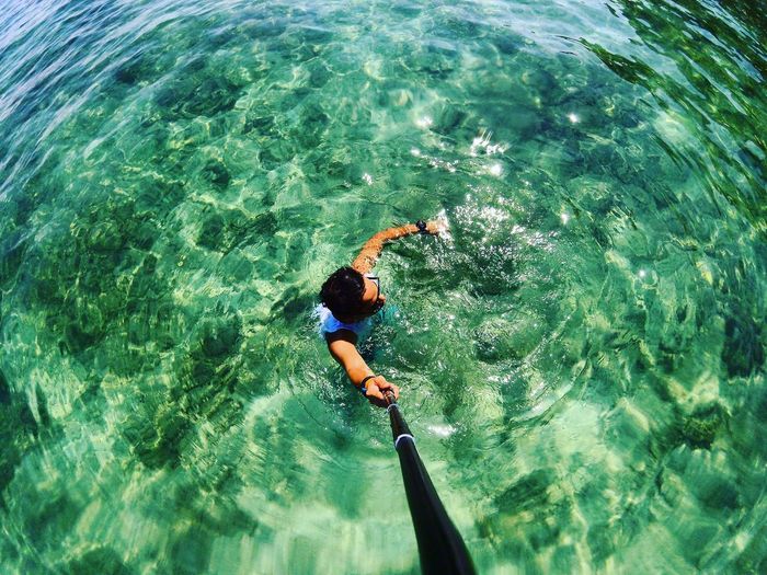 High angle view of man holding monopod while swimming in sea