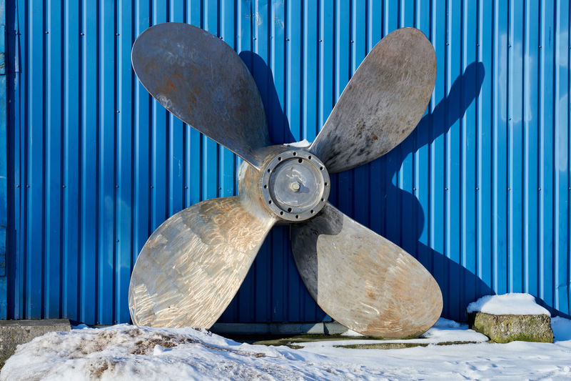 Old boat propeller deteriorate in boat yard in winter. rusty ship propeller on blue wall background.