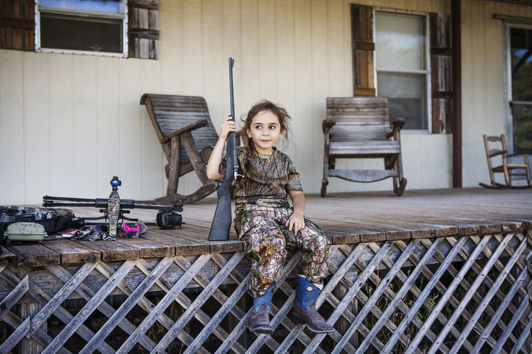 Girl holding rifle while sitting on porch