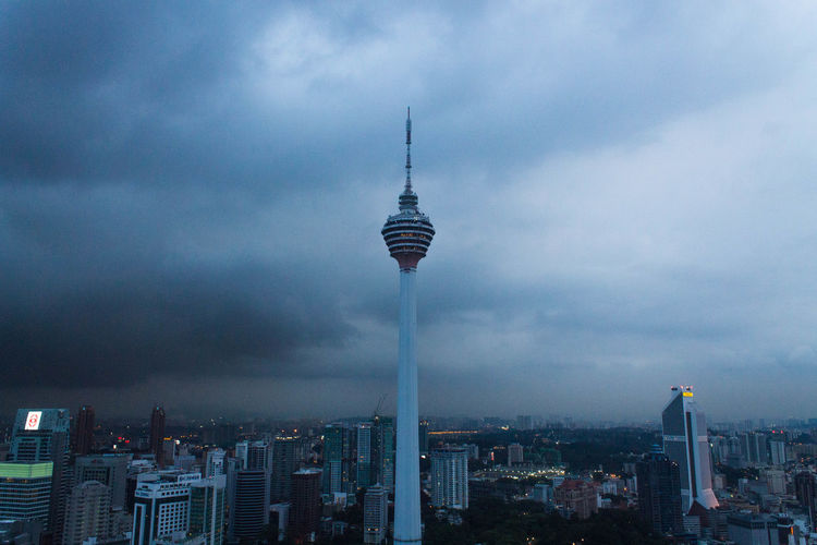 Communications tower in city against cloudy sky