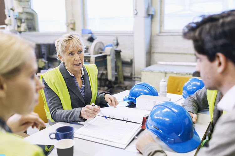 Mature female worker having discussion with colleagues at table in factory