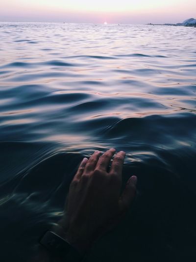 Person hand on sea against sky during sunset