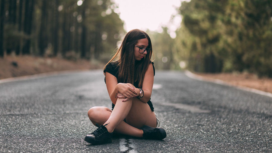 Young woman sitting on road against trees