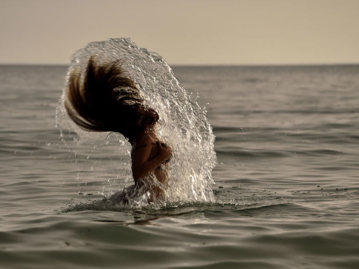 Side view of woman tossing wet hair in sea during sunset