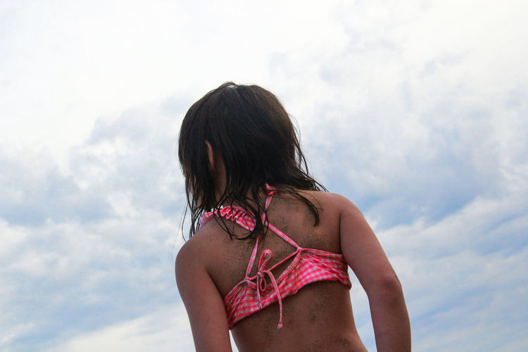 Rear view of girl in bikini standing against sky