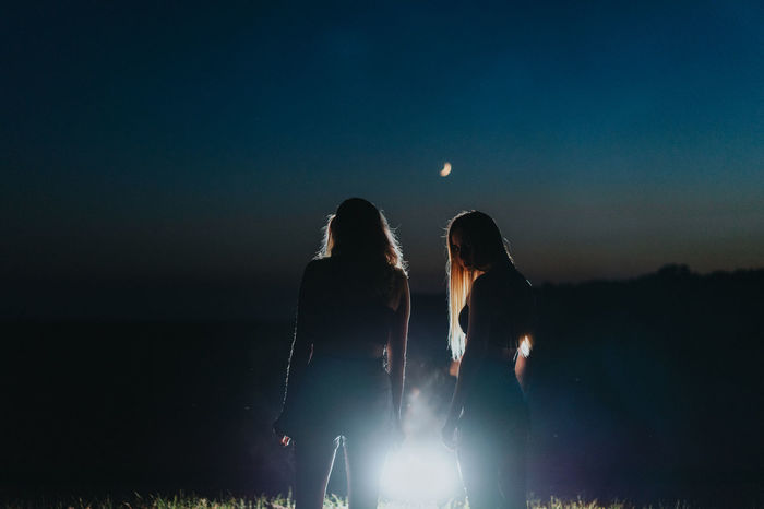 Silhouette women standing against illuminated background against sky during dusk