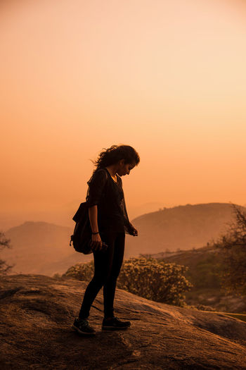 Side view of woman standing on mountain against clear sky during sunset