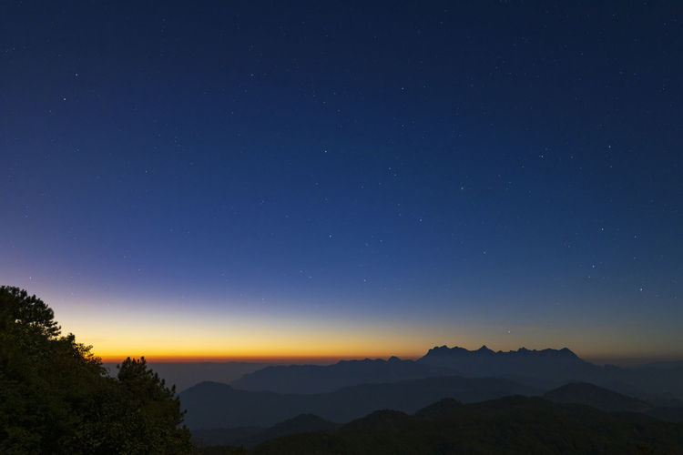 Scenic view of silhouette mountains against blue sky at night