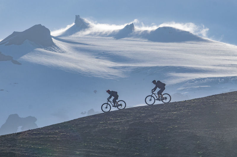 Men riding bicycle on mountain against sky