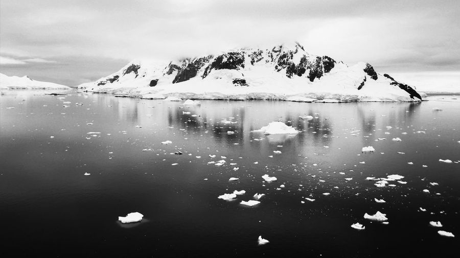 Black and white photo of sea with icebergs against snowcapped mountains in antarctica
