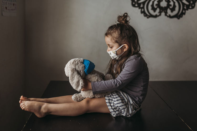 Side view of young girl with mask on sitting with masked animal negative space