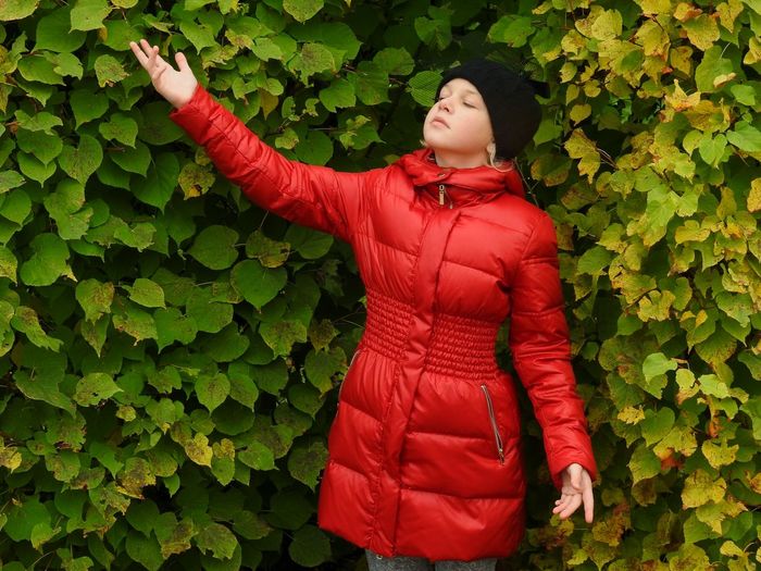 Girl in red jacket standing against plants