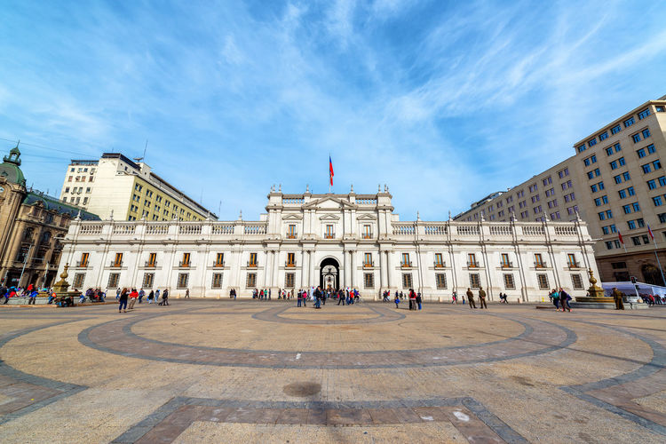 Low angle view of people at la moneda palace against blue sky during sunny day
